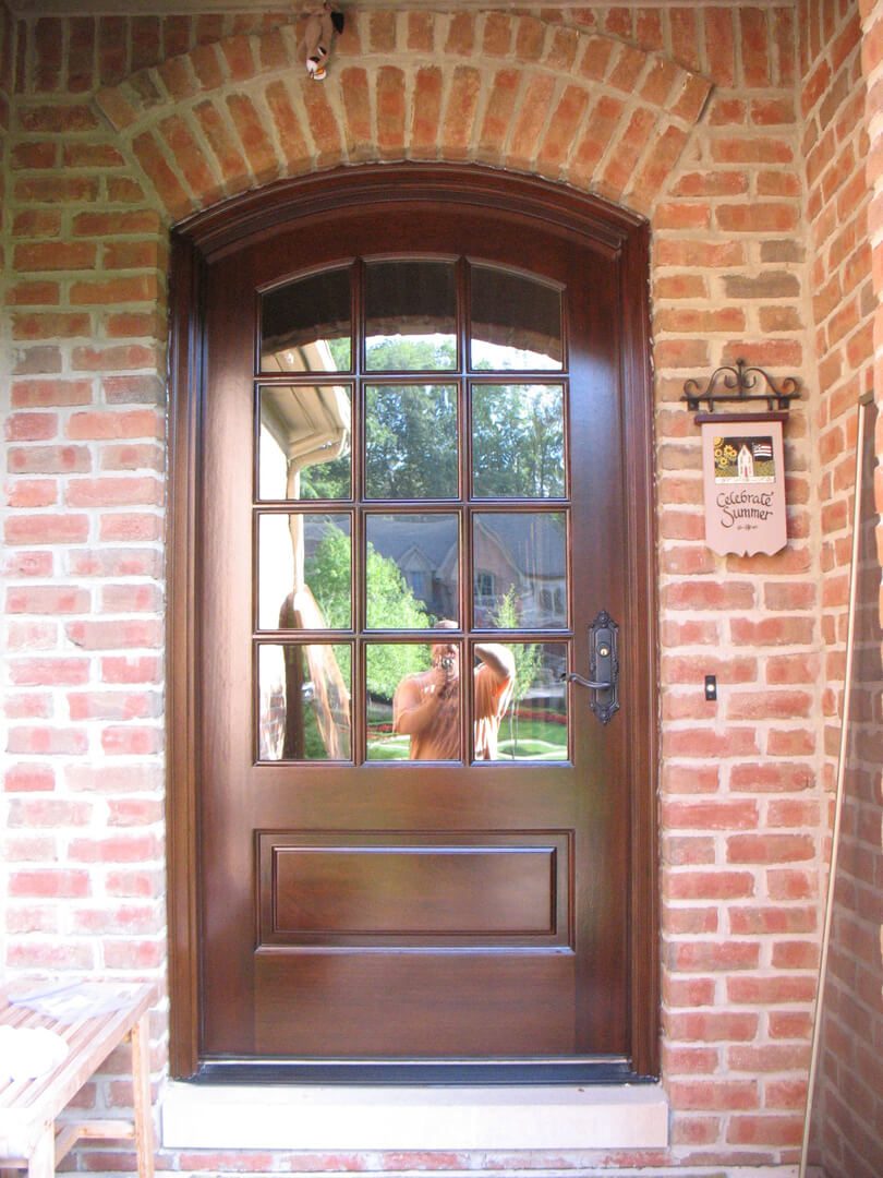 A door with a window in it and a dog sitting on the porch.