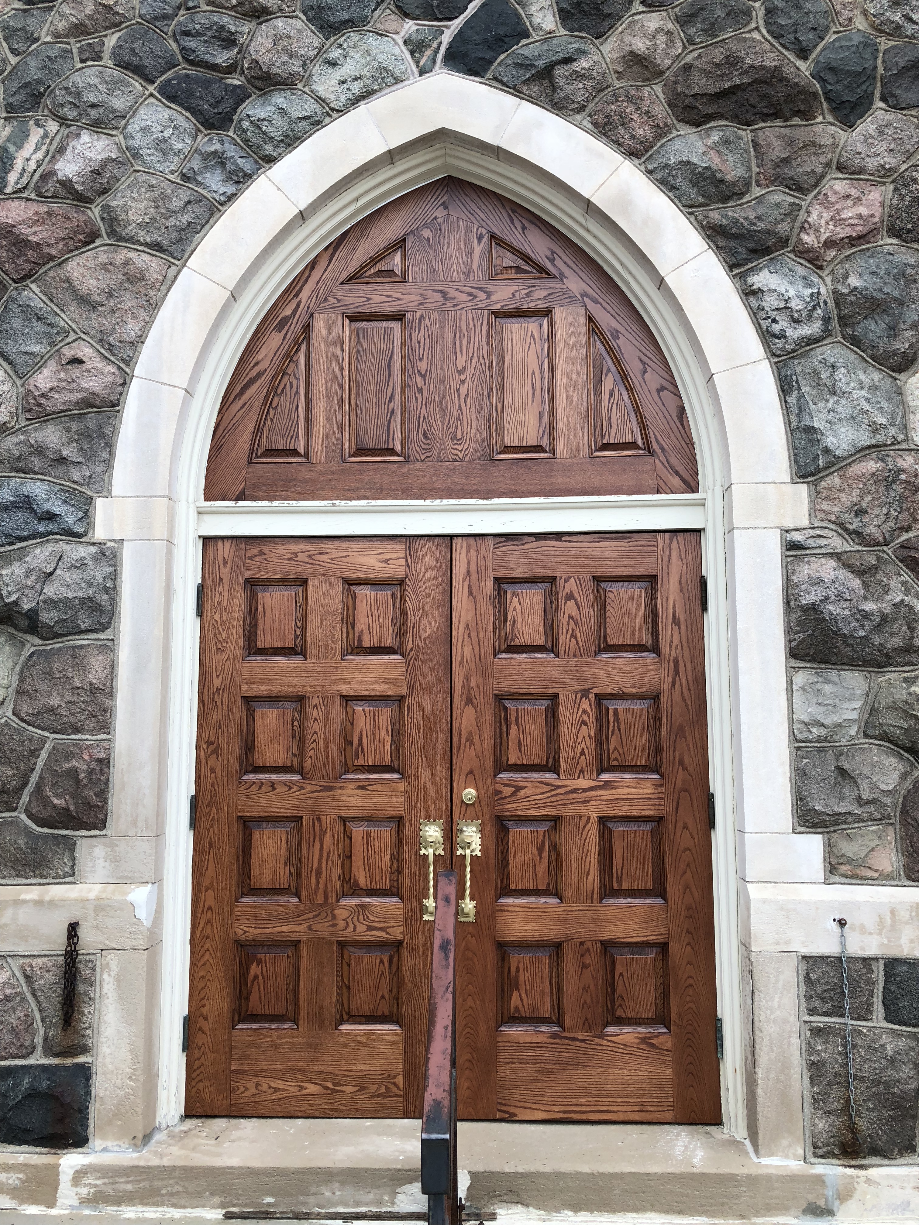 A church door with two wooden doors and a stone wall.