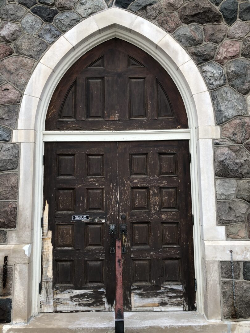 A church door with two wooden doors and a stone wall.
